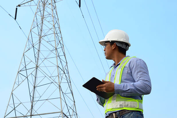 Survey engineer in a hard hat inspecting a transmission tower